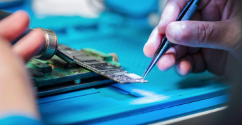 Hands holding tools repairing a circuit board.